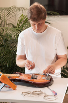 Young technician installing control knobs on a repaired bass guitar