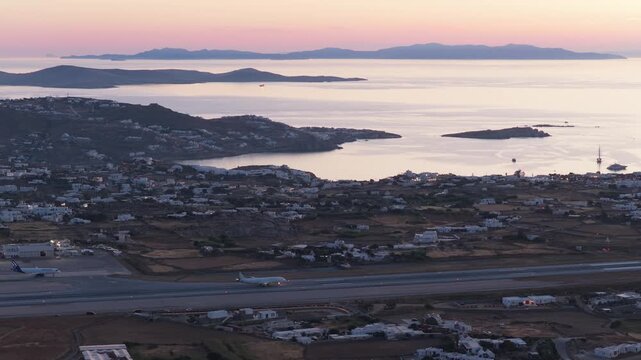 Commercial passenger airplane landing at Mykonos Island National Airport JMK runway at dusk with panoramic scenery of Aegean Sea and Cyclades islands in Greece