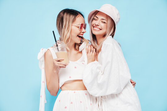 Two young beautiful smiling blond hipster female in trendy summer clothes. Carefree women posing near blue wall in studio. Positive models having fun. Cheerful and happy
