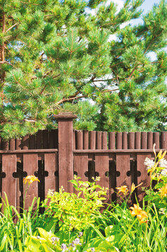 Rustic wooden fence with decorative pattern stands amid lush leaves