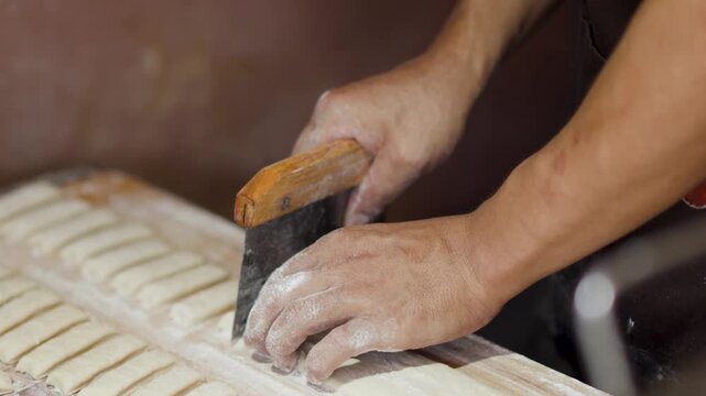 Asian Chef Slicing Dough Strips with Bench Scraper in Bakery