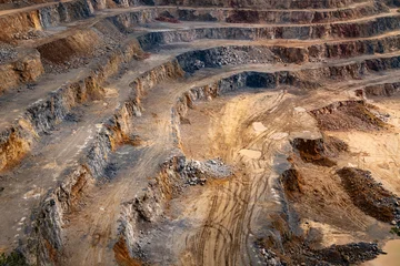 A view into a large limestone quarry in Hagen-Hohenlimburg (Germany) with several levels or benches. A gray-brown rocky landscape with blasted debris and rubble, and access roads for excavators and tr © ON-Photography