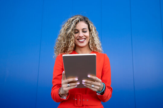Portrait of young woman wearing red dress in front of blue background using digital tablet