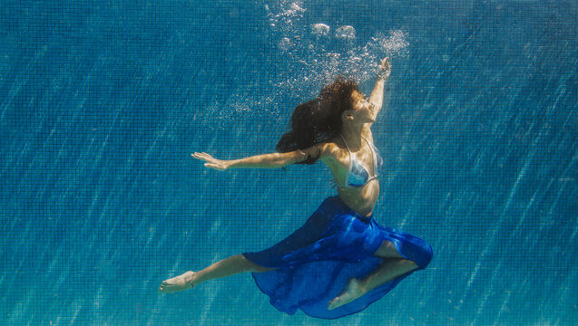 A woman wears a floral dress underwater in a swimming pool