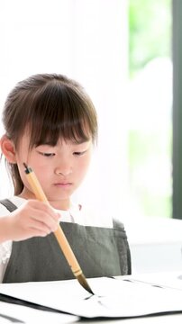 書道に集中して筆で文字を書く小学生の女の子・習字を学ぶ日本の子どものクローズアップの縦動画