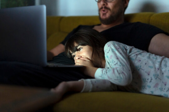Happy daughter and father looking at laptop on couch at night