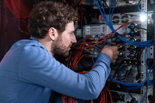 Male IT professional connecting cable in server rack at data center