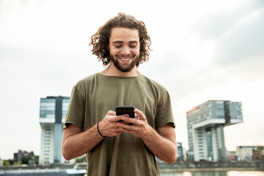 Germany, Cologne, smiling young man looking at cell phone