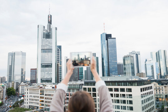 Germany, Hesse, Frankfurt, woman taking a picture of the skyline with mini tablet