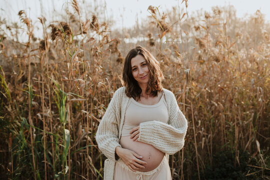Smiling expectant mother holding her baby bump outdoors