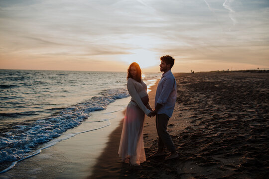 Expecting couple holding hands on the beach at sunset