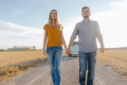 Young couple walking on dirt track at camper van in rural landscape