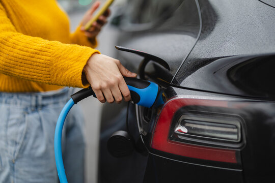 Woman charging car through electric plug at station