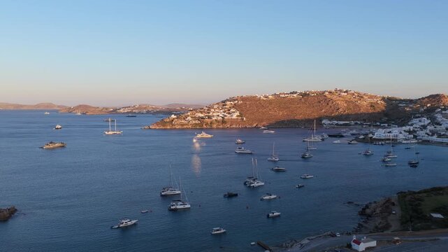 Mykonos, Greece summer sunset revealing Ornos Beach with luxury yachts and catamarans anchored in calm Aegean Sea bay, Cycladic island lifestyle