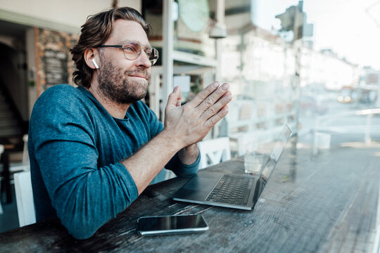 Smiling manwith hands clasped by laptop in cafe