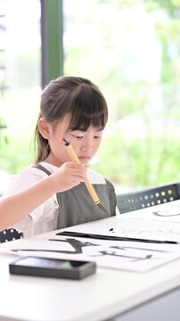 書道に集中して筆で文字を書く小学生の女の子・習字を学ぶ日本の子どものクローズアップの縦動画