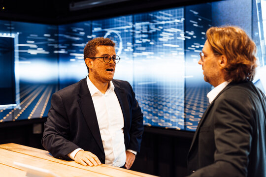 Colleagues discuss business in a television studio with a screen