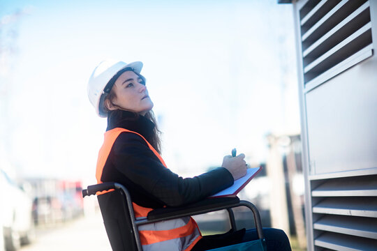Young technician with safety helmet and vest in wheelchair working outdoors