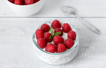 Delicious raspberry chia pudding on a white wooden background.Healthy layered chia seed pudding topped with fresh red raspberries and a mint leaf in a transparent glass bowl. Served on a white wooden  © Margo