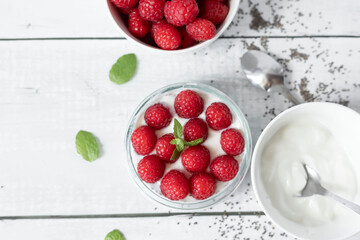 Delicious raspberry chia pudding on a white wooden background.Healthy layered chia seed pudding topped with fresh red raspberries and a mint leaf in a transparent glass bowl. Served on a white wooden  © Margo