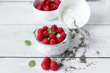 Delicious raspberry chia pudding on a white wooden background.Healthy layered chia seed pudding topped with fresh red raspberries and a mint leaf in a transparent glass bowl. Served on a white wooden  © Margo