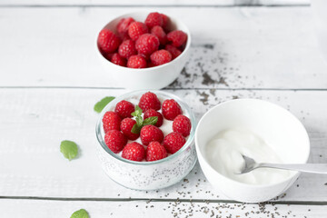 Delicious raspberry chia pudding on a white wooden background.Healthy layered chia seed pudding topped with fresh red raspberries and a mint leaf in a transparent glass bowl. Served on a white wooden  © Margo