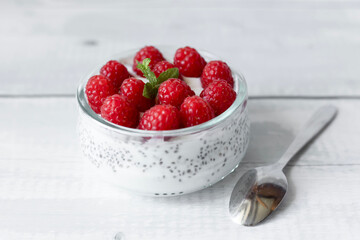 Delicious raspberry chia pudding on a white wooden background.Healthy layered chia seed pudding topped with fresh red raspberries and a mint leaf in a transparent glass bowl. Served on a white wooden  © Margo