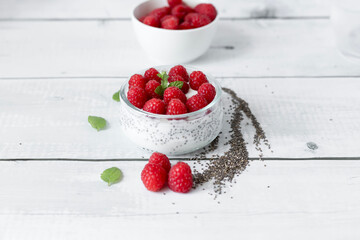 Delicious raspberry chia pudding on a white wooden background.Healthy layered chia seed pudding topped with fresh red raspberries and a mint leaf in a transparent glass bowl. Served on a white wooden  © Margo