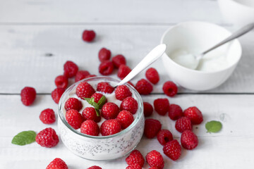 Delicious raspberry chia pudding on a white wooden background.Healthy layered chia seed pudding topped with fresh red raspberries and a mint leaf in a transparent glass bowl. Served on a white wooden  © Margo