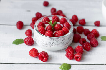 Delicious raspberry chia pudding on a white wooden background.Healthy layered chia seed pudding topped with fresh red raspberries and a mint leaf in a transparent glass bowl. Served on a white wooden  © Margo