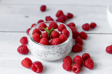 Delicious raspberry chia pudding on a white wooden background.Healthy layered chia seed pudding topped with fresh red raspberries and a mint leaf in a transparent glass bowl. Served on a white wooden  © Margo