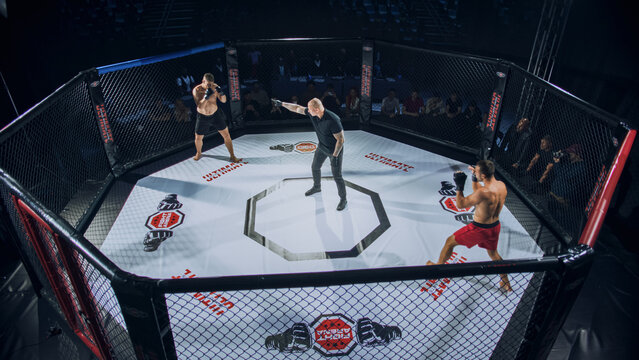 Two Athletic MMA Fighters Fight Square Off in Cage Fight as Referee Signals the Start of Action, With a Loud Crowd Around the Octagon Watching, High-stakes Combat Sports Event.