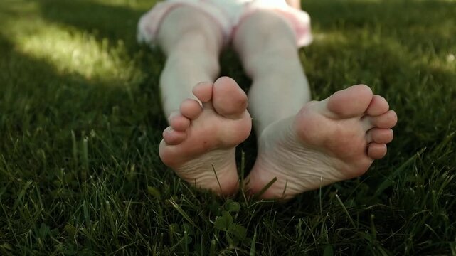 Adult woman's bare feet resting on a lush, vibrant green grass lawn. Soft summer sunlight highlights the soles and toes as she gently moves and relaxes, evoking a sense of mindfulness, grounding