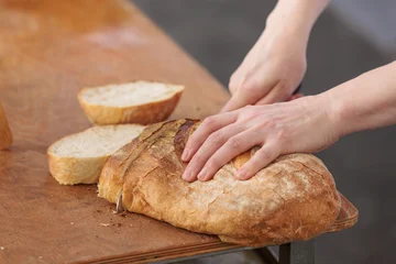 Hands cutting a fresh artisan bread loaf into thick slices on a table © uv_group