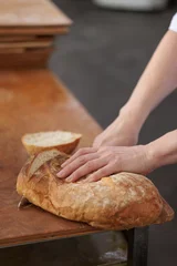 Baker slicing a large rustic artisan bread loaf on a wooden worktable © uv_group