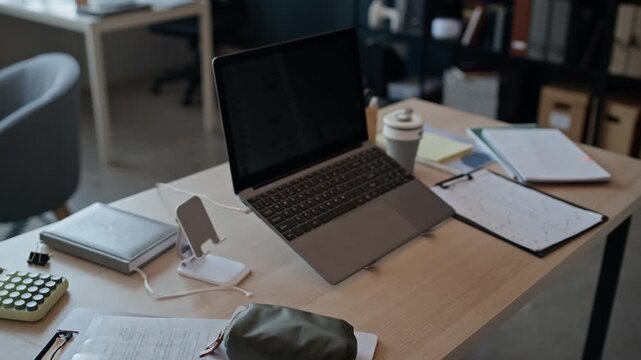 No people shot of laptop computer on stand on wooden office desk next to notebooks, calculator and documents. Empty workspace representing remote work, corporate business or digital education concepts