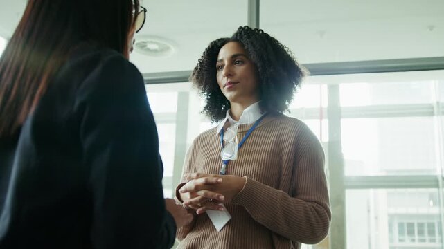 Two professional women engage in a conversation at an event or office. One woman attentively listens to the other, conveying connection and communication.