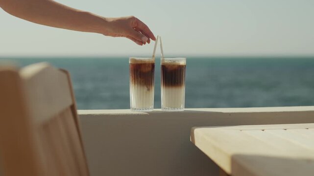 Two iced drinks on a table with ocean view and sunlight