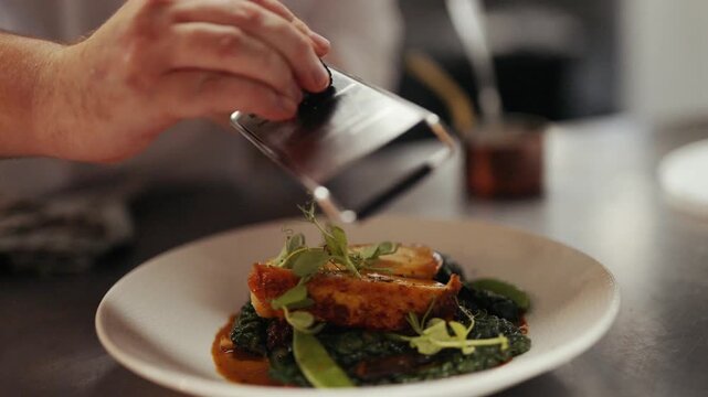 Chef pours sauce onto a beautifully plated dish in a hotel kitchen