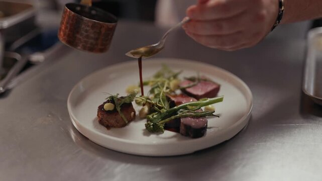 Chef finishes plating a gourmet dish with sauce in a professional kitchen