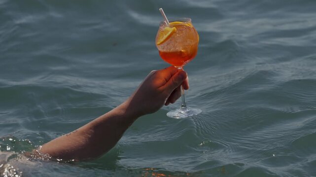 Orange cocktail in a glass floats in turquoise ocean water