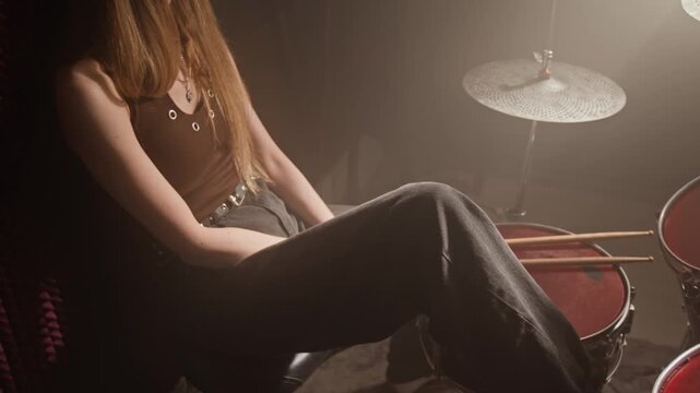 Tired young woman sitting at drum kit in recording studio with closed eyes, preparing to play. Footage for music school promos or instrument retail advertisements