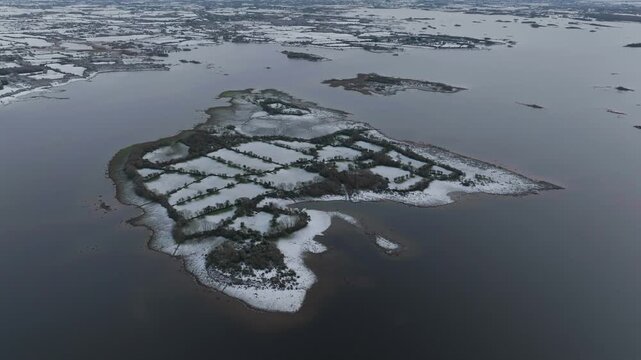 A cinematic drone shot capturing a snowcovered island with traditional stone walls in Lough Corrib, Galway, Ireland during winter.