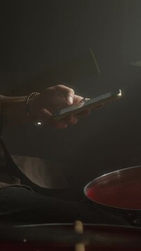 Vertical video of male drummer using smartphone while sitting at drum kit. Clip for promoting music learning apps or digital entertainment services