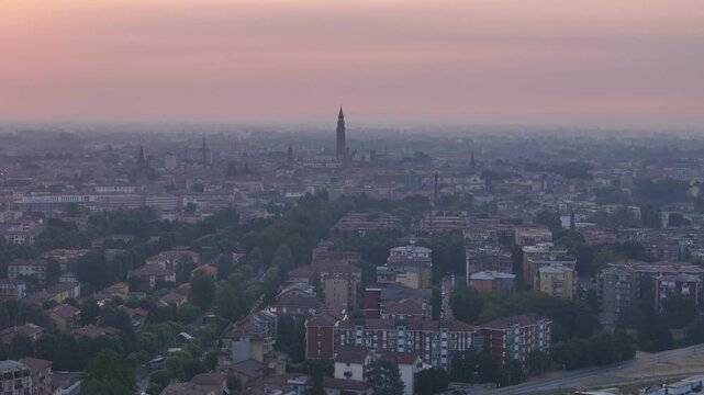 Torrazzo and Cattedrale di Santa Maria Assunta rise above Cremona at sunrise during the 2026 summer heatwave, softened by atmospheric haze across Lombardy, Italy, slow drone pullback.