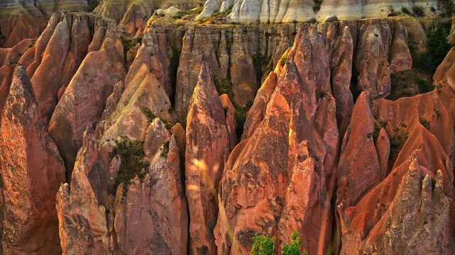 A high-angle shot of the unique geological formations in Cappadocia, Turkey, featuring layered volcanic tuff rocks, traditional fairy chimneys, and green vegetation in the valley. 2