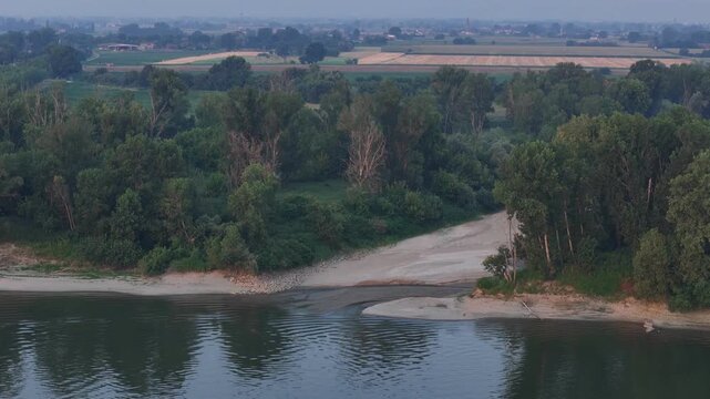 Dry secondary channel cuts through the Po River floodplain near Castelvetro Piacentino, Piacenza, Emilia-Romagna, Italy, exposing sediments after the 2026 summer drought, slow drone pullback.