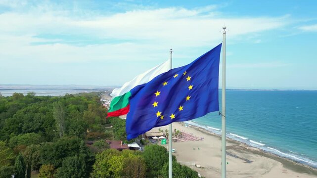 The drone slowly rotates around the Bulgarian and European Union flags in slow motion above the coast of Burgas, Bulgaria.