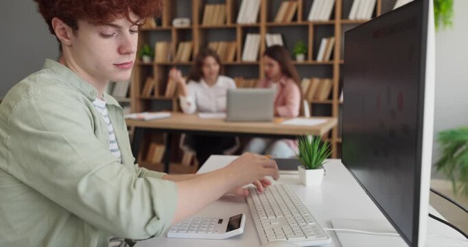Teenager student using computer in classroom with charts. Screen shows data while a calculator supports analysis and research for a school project. Education. Theme of digital literacy skills.