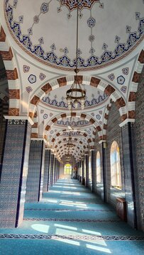 Long corridor inside a Turkish mosque adorned with traditional Ottoman motifs. The ceiling features intricate patterns with blue and brown geometric designs. 